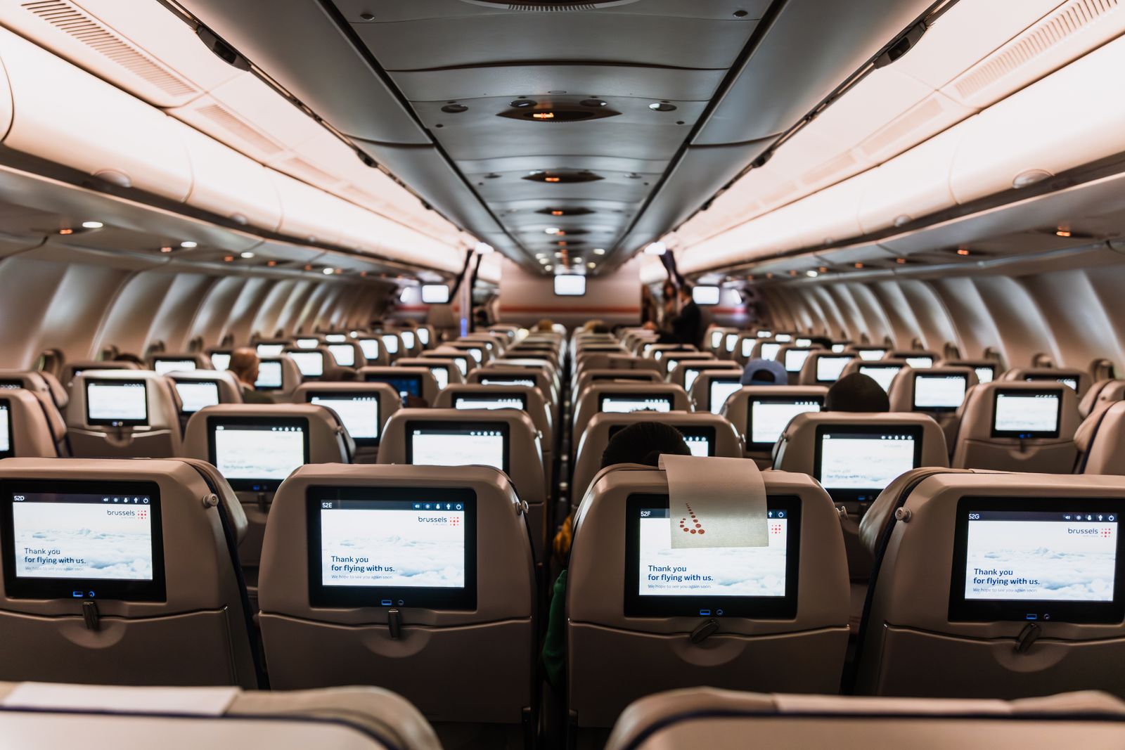 Inside a modern commercial aircraft cabin, looking down the aisle past rows of seatback entertainment screens