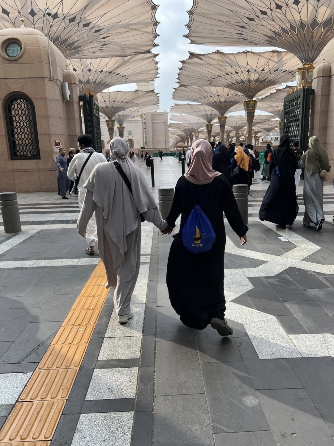 Sisters of a past journey holding hands under the umbrellas of Masjid an-Nabawi